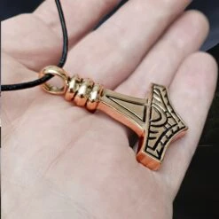 Large Bronze Gotland Replica Thors Hammer Pendant -The Viking Dragon Shop sn bronze large gotland hammer front side angle view on hand on leather thong